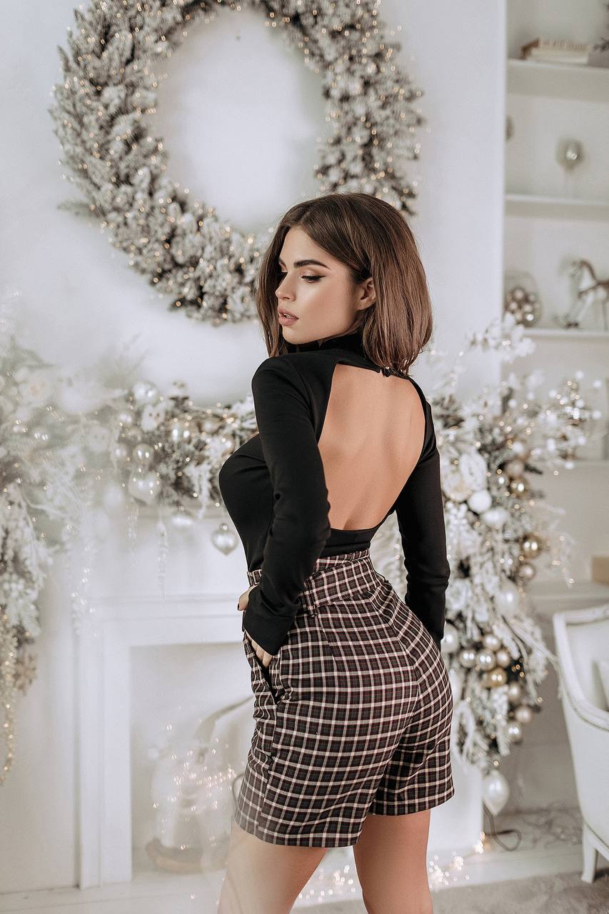 Woman in a black top and plaid skirt standing in a decorated room with wreaths and lights.