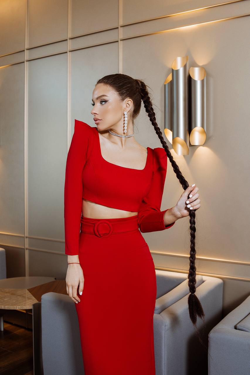 Woman in a red outfit holding a long braid in an elegant interior setting