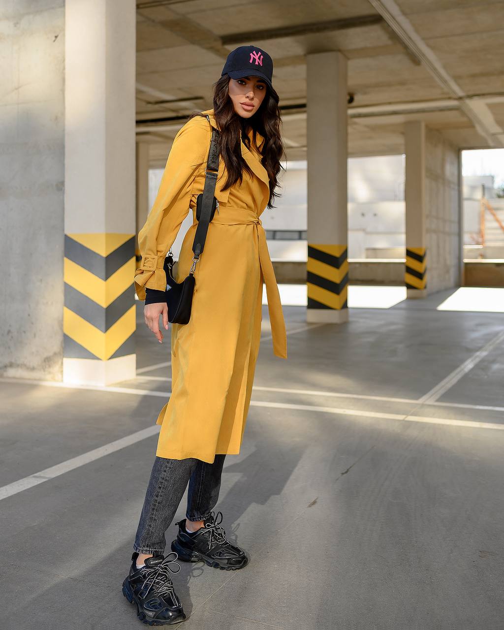 Woman in a yellow trench coat standing in an underground parking lot.