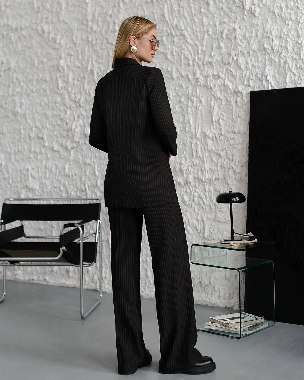 Person wearing a black suit standing in a modern room with a textured white wall.