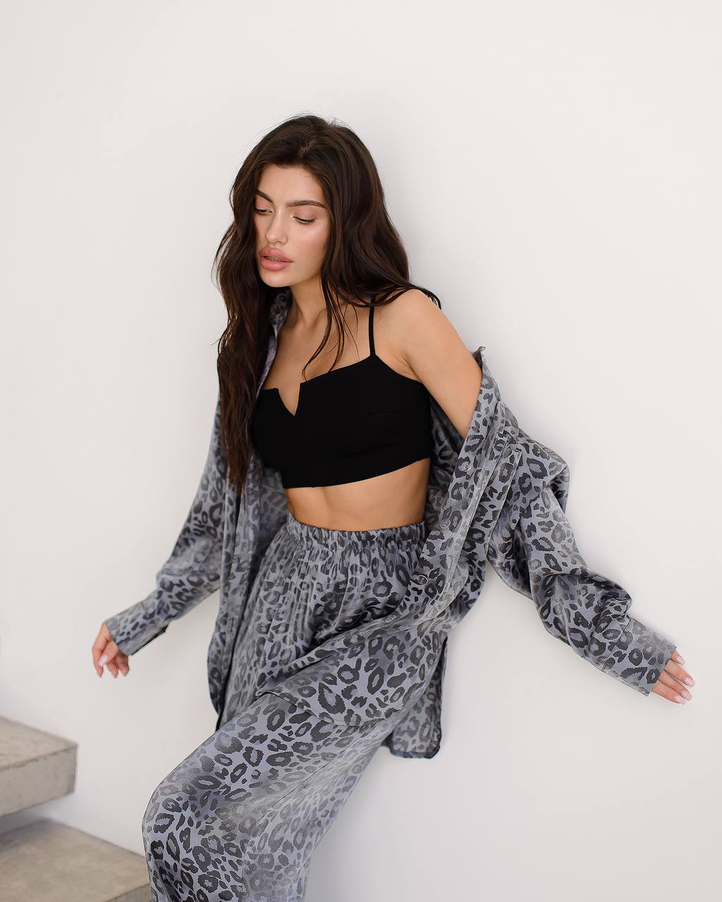 Woman wearing a black top and gray leopard print pants with a matching cardigan against a white background