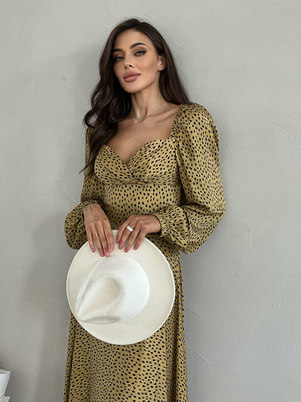 Woman in a patterned dress holding a white hat against a plain background