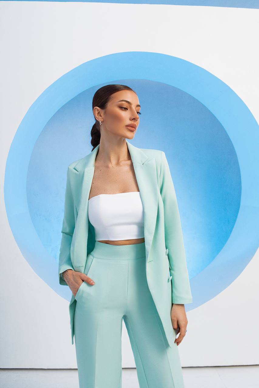 Woman in a light green suit standing against a white background with blue circular design