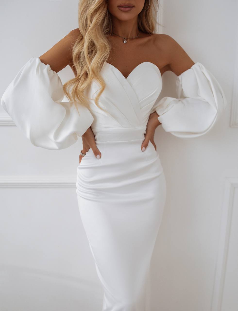 Woman wearing a white off-shoulder dress with puffed sleeves against a plain background