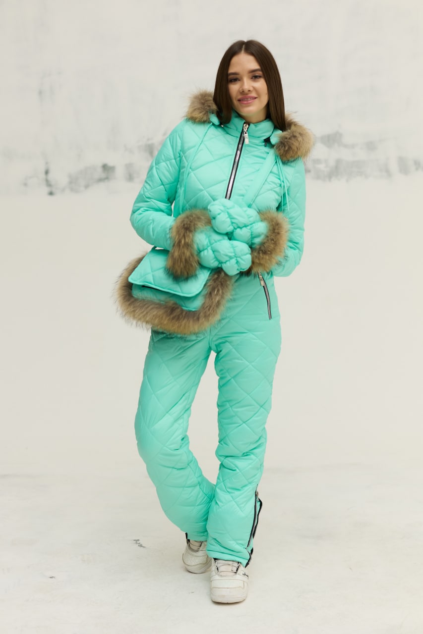 Person wearing a teal puffer suit with fur trim against a white background