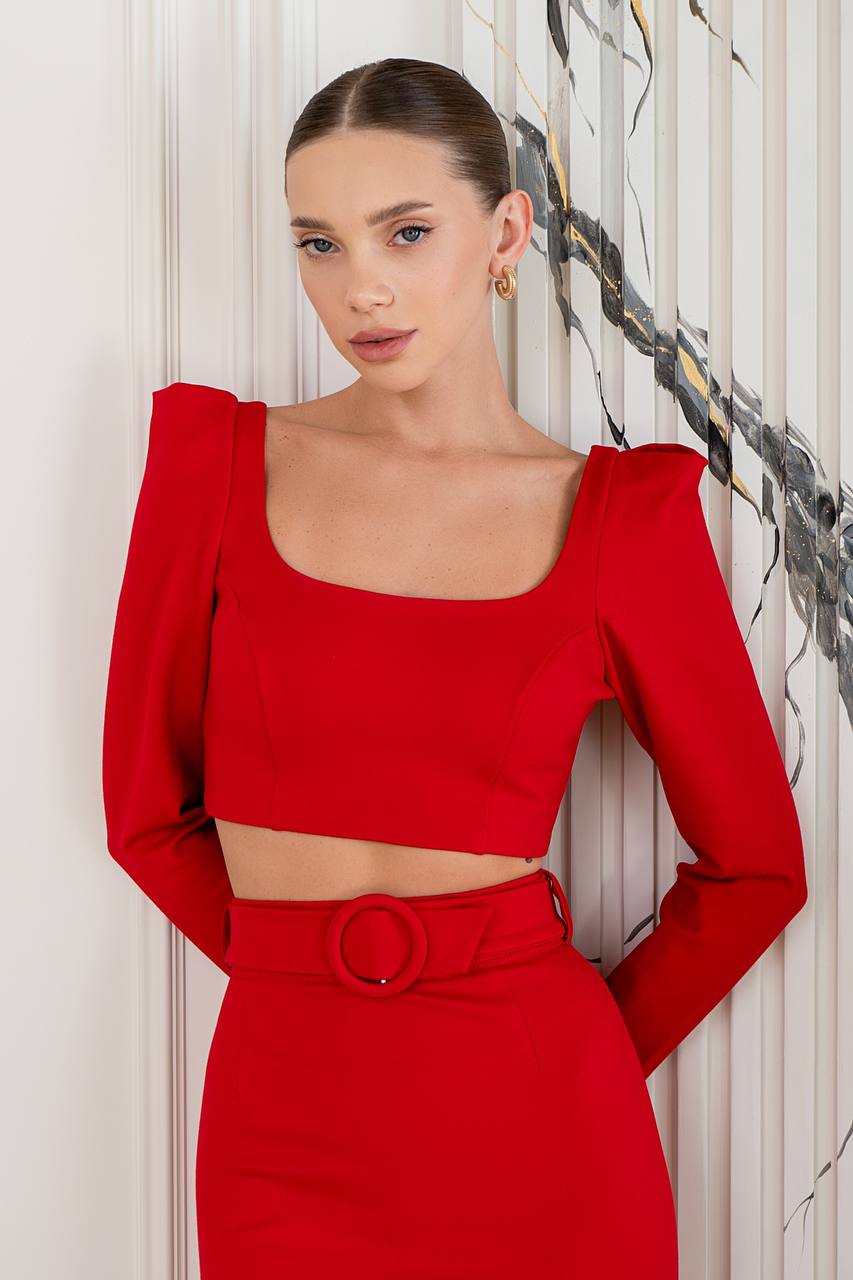 Woman wearing a red outfit with a belt against a decorative wall.