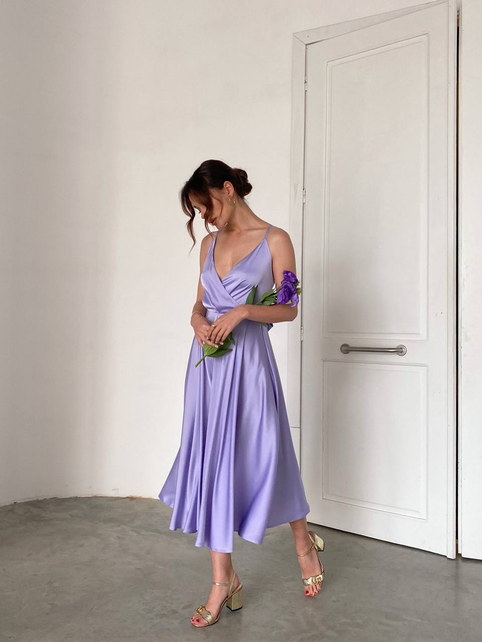 Woman in a lavender dress holding flowers in a minimal indoor setting