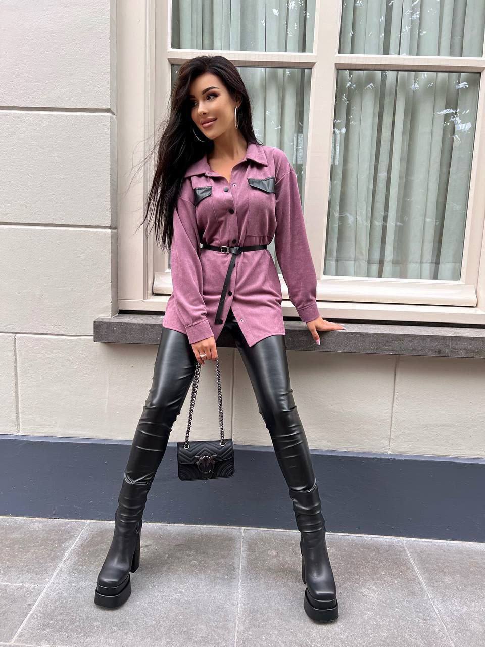 Woman in pink shirt and black leather pants standing on a sidewalk.