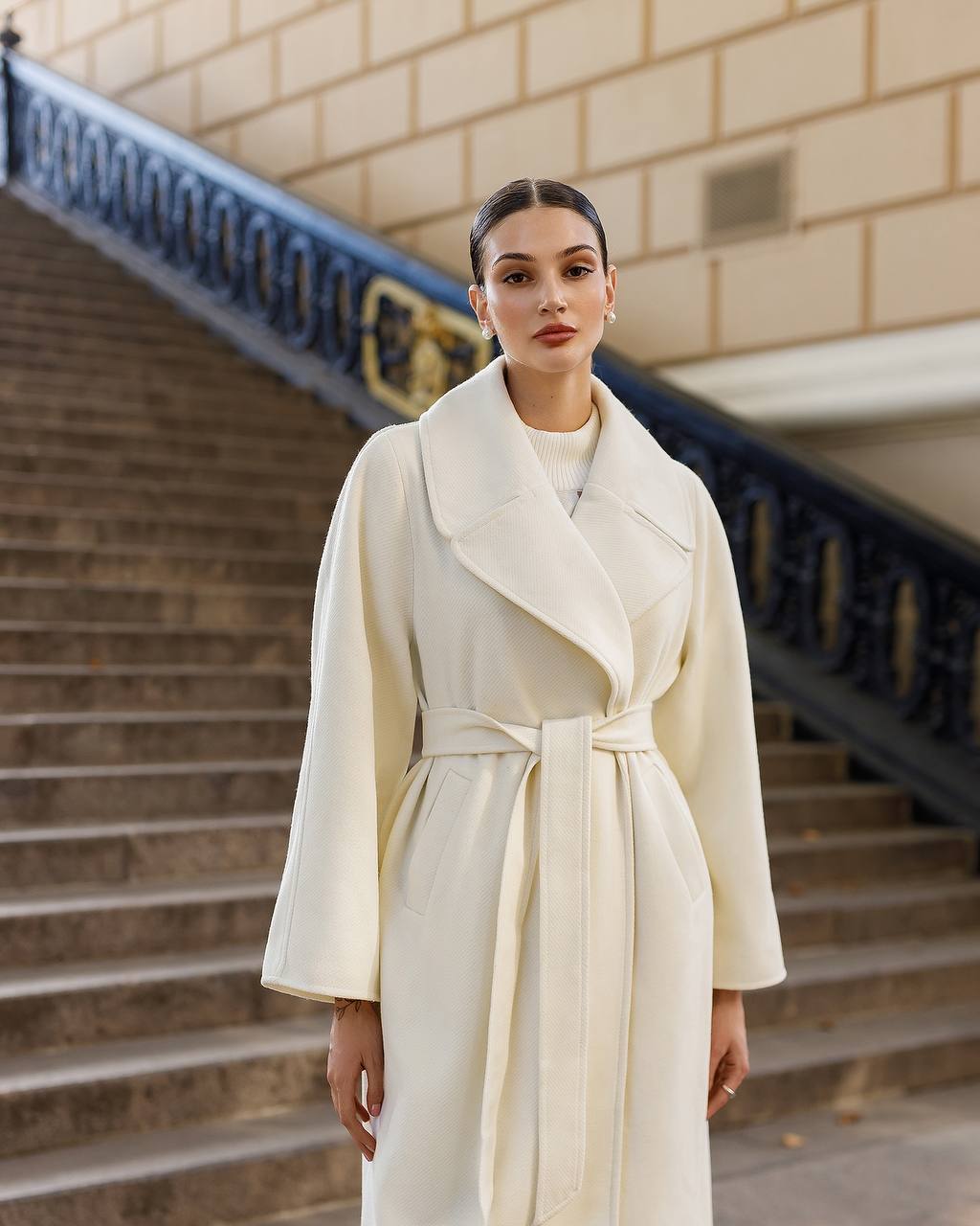Woman wearing a white coat standing on steps with a building in the background