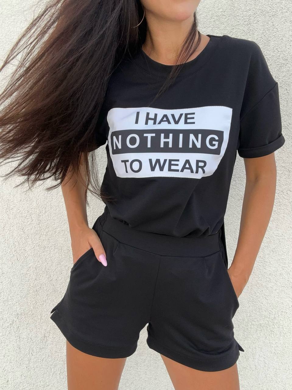 Person wearing a black t-shirt with 'I HAVE NOTHING TO WEAR' text and black shorts against a light background