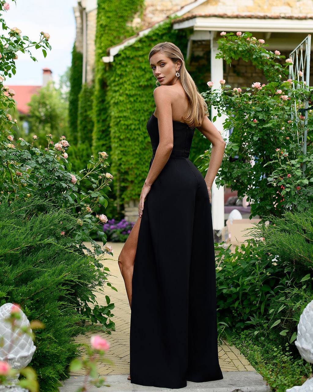 Woman in a black dress with a slit standing in a garden.