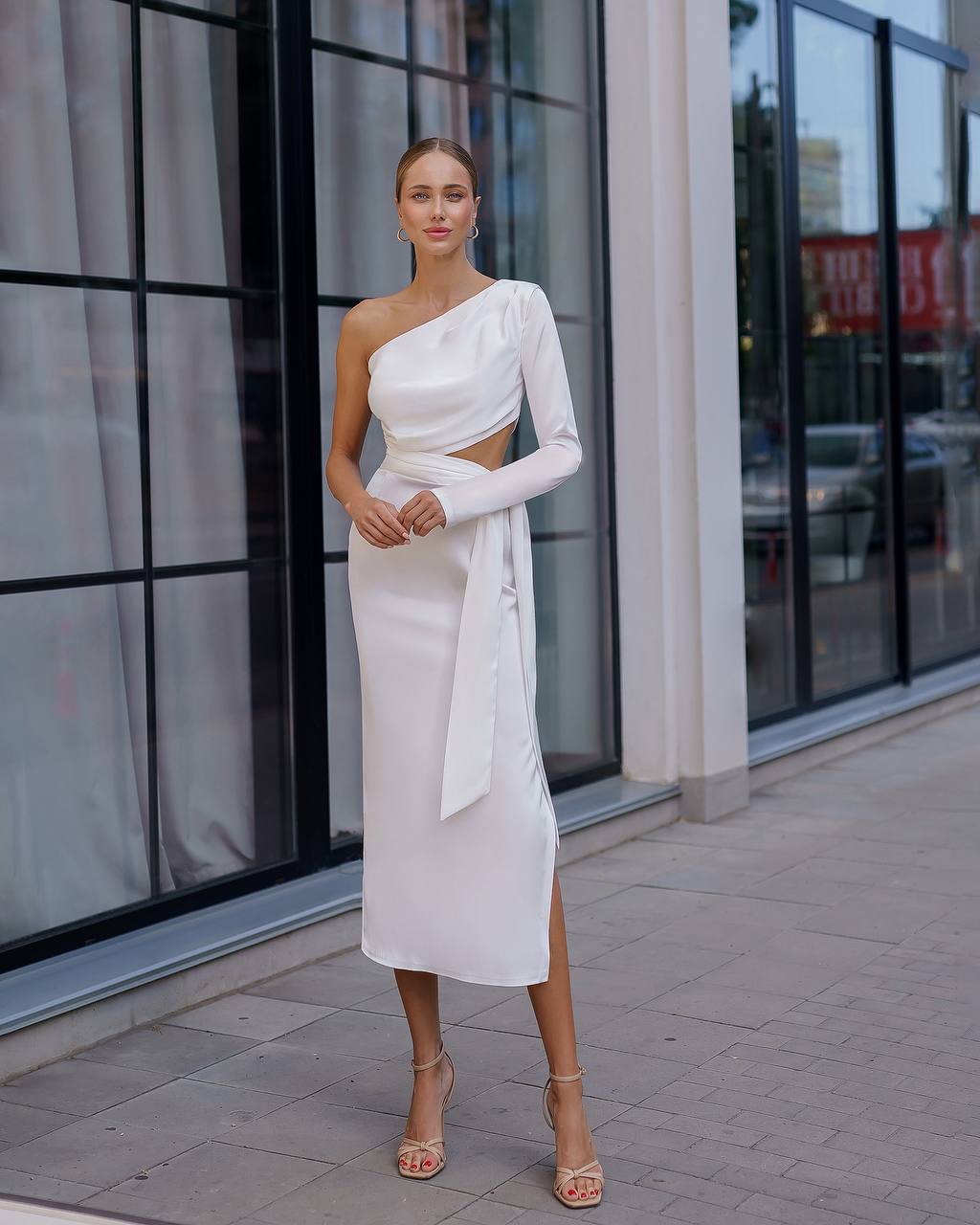Woman wearing a white one-shoulder dress standing on a city street.