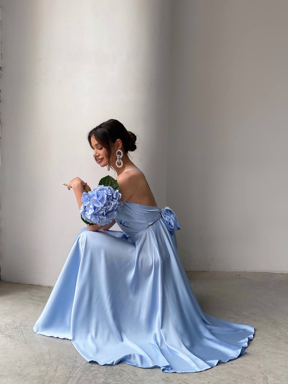 Woman in a light blue off-shoulder gown holding flowers against a plain background