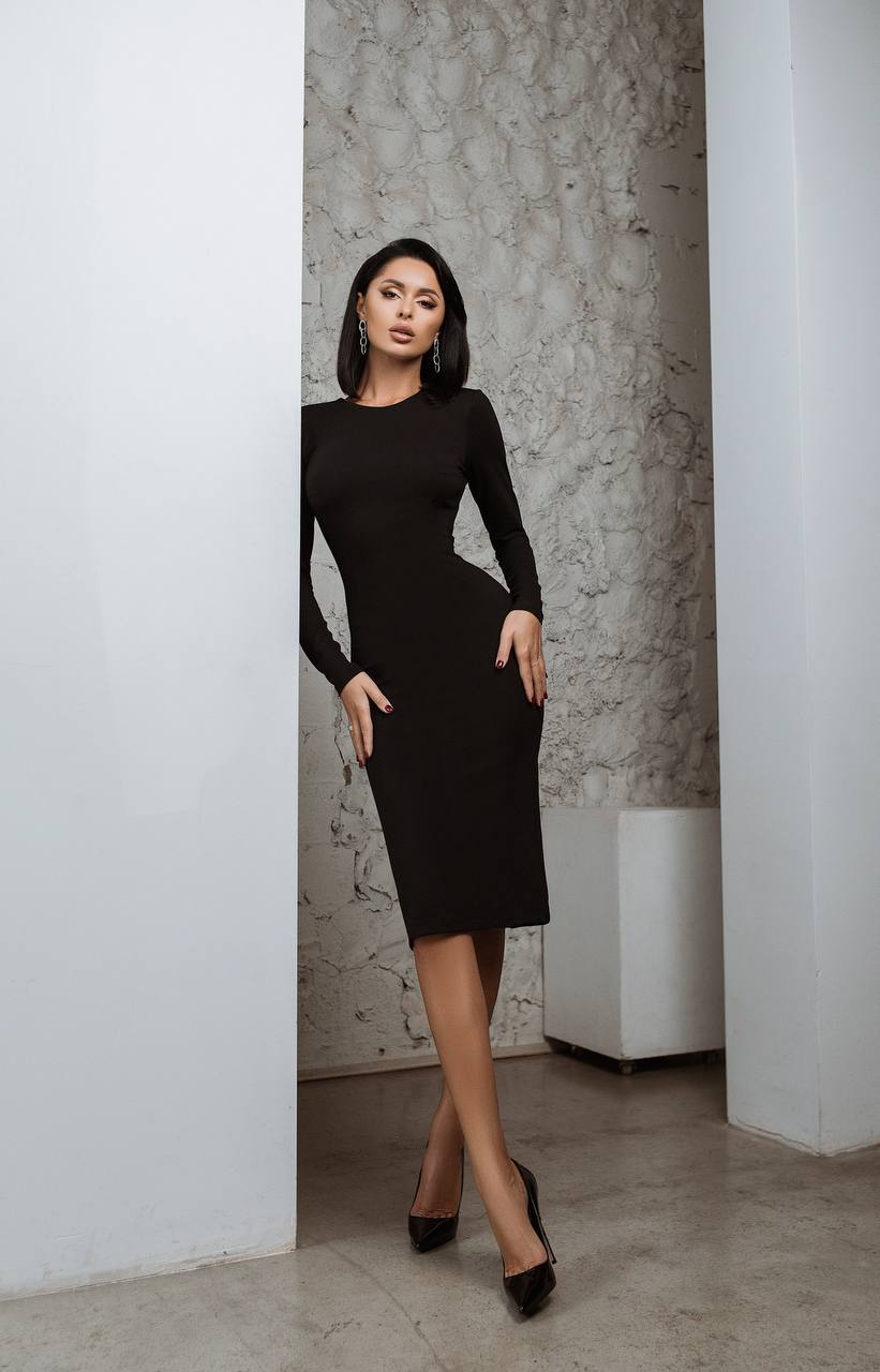 Woman wearing a black dress standing against a textured wall.