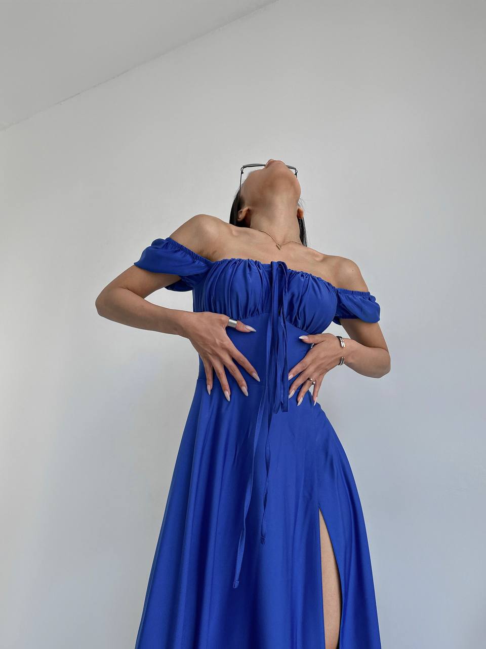 Woman wearing a blue off-shoulder dress with a slit on a plain background