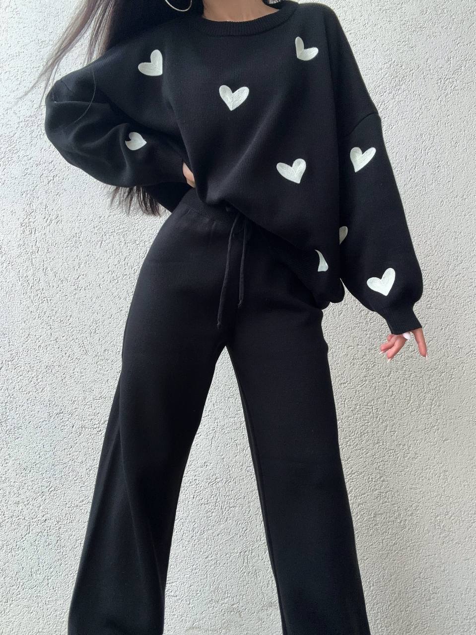 Person wearing a black sweater with white heart patterns against a light gray background