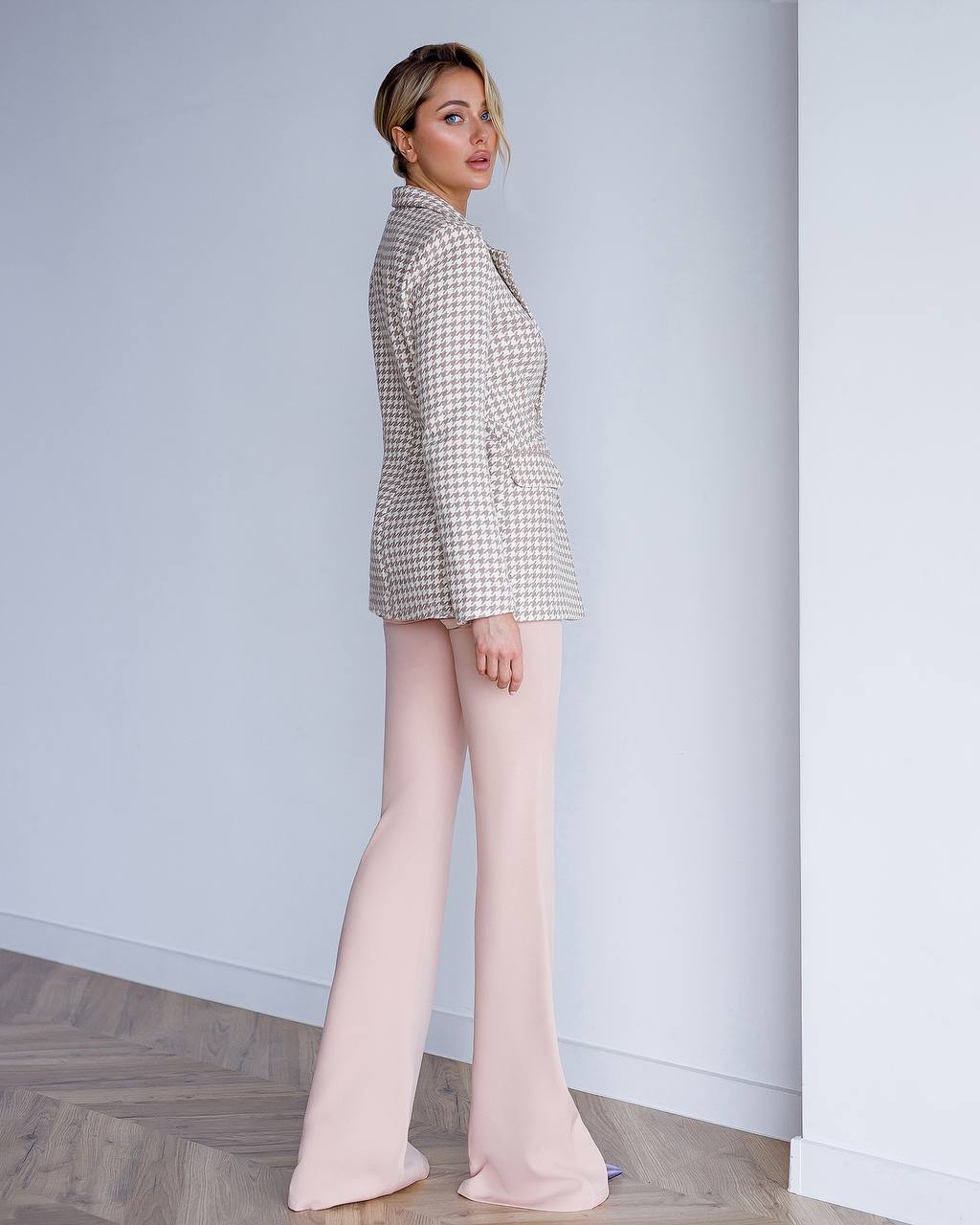 Woman wearing a checkered blazer and light pink pants against a plain background