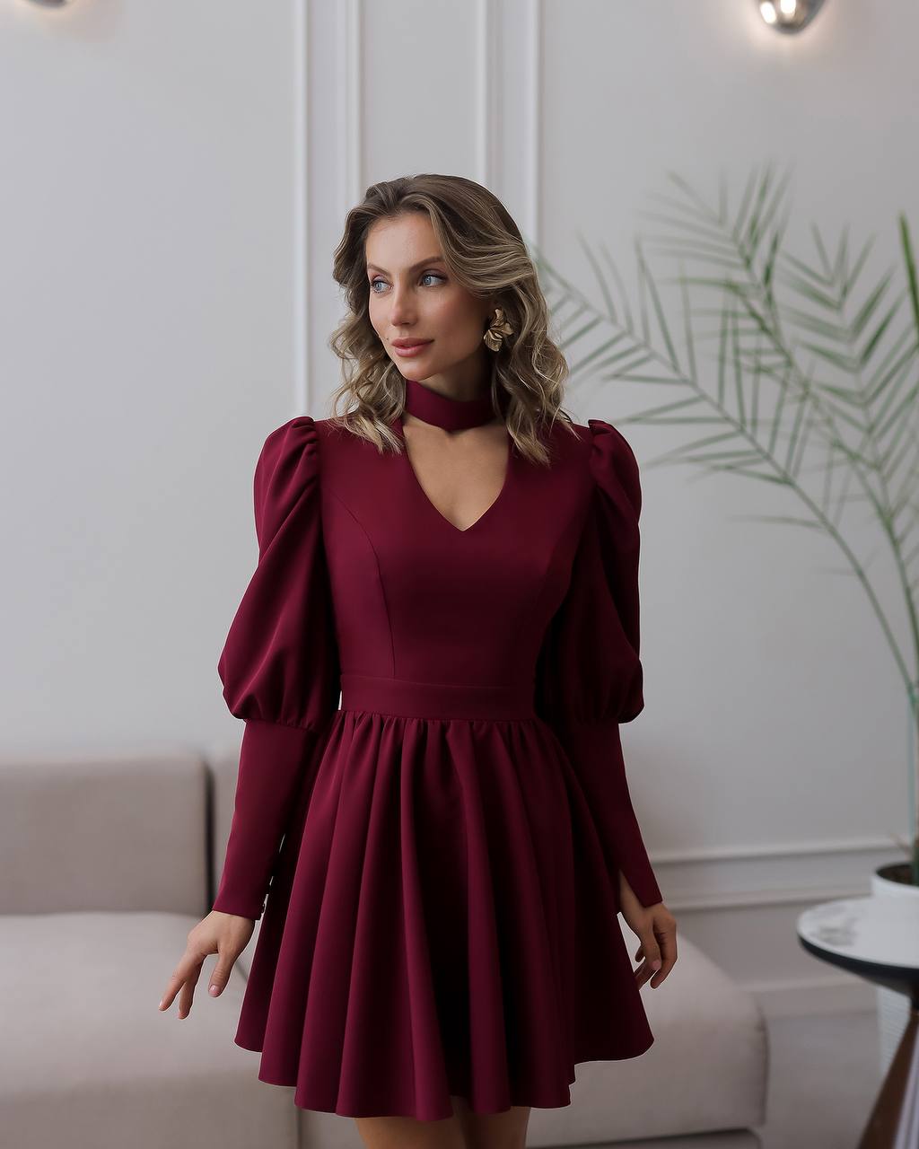 Woman wearing a burgundy dress with puffed sleeves in an indoor setting.