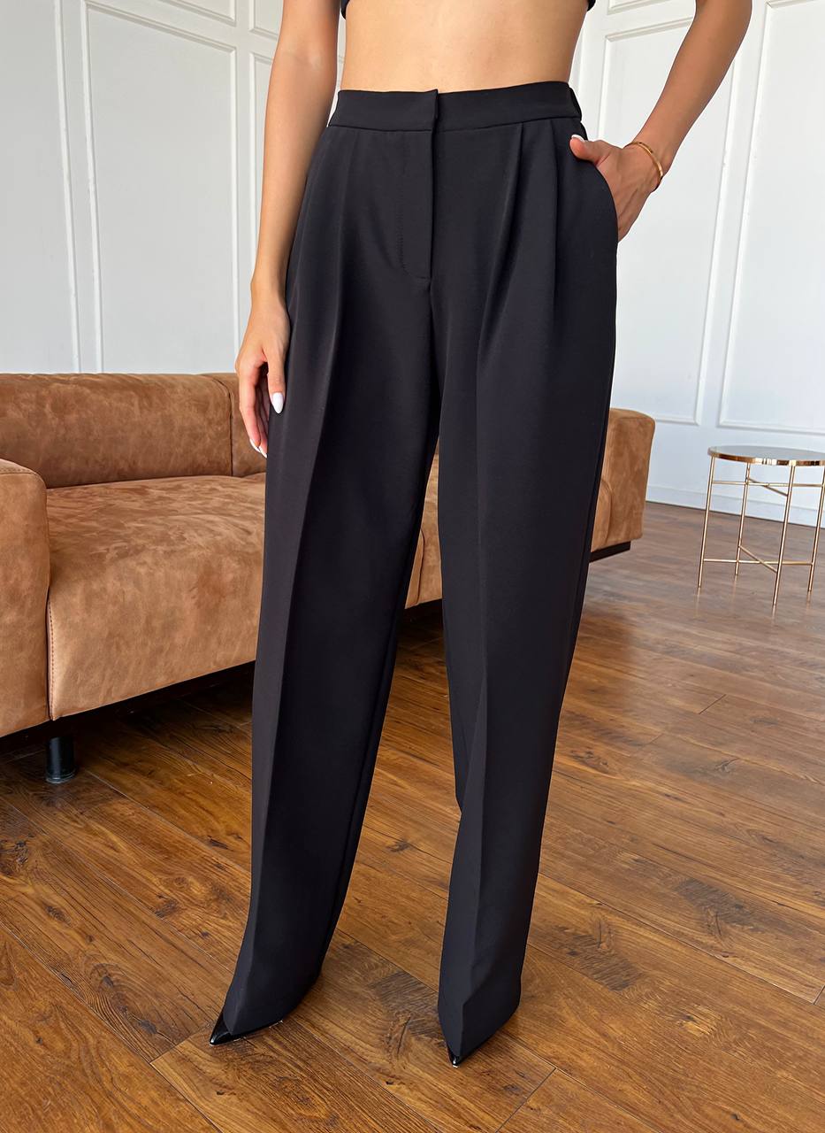 Person wearing black high-waisted pants in a room with wooden flooring and a brown couch.