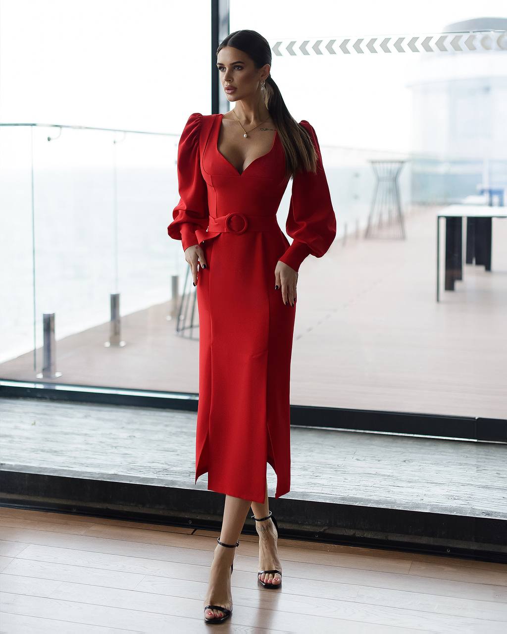 Woman in a red dress standing in a modern indoor setting with large windows.