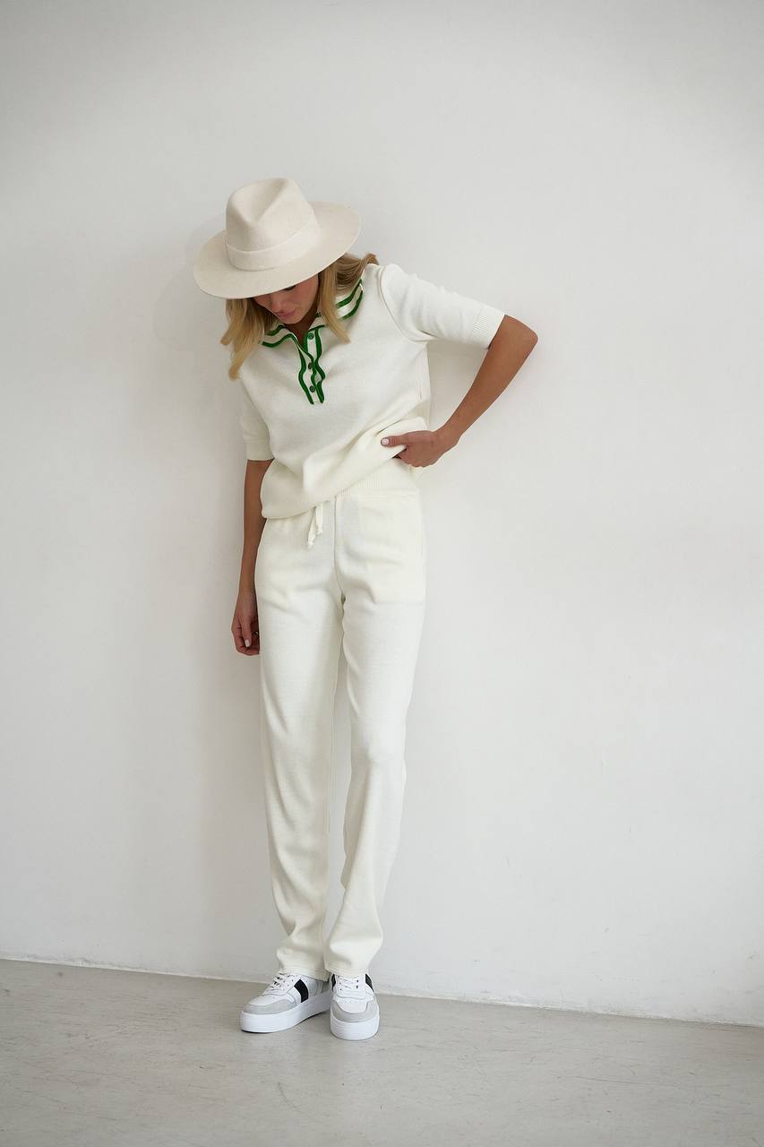 Person wearing a white outfit with a hat and sneakers against a plain background