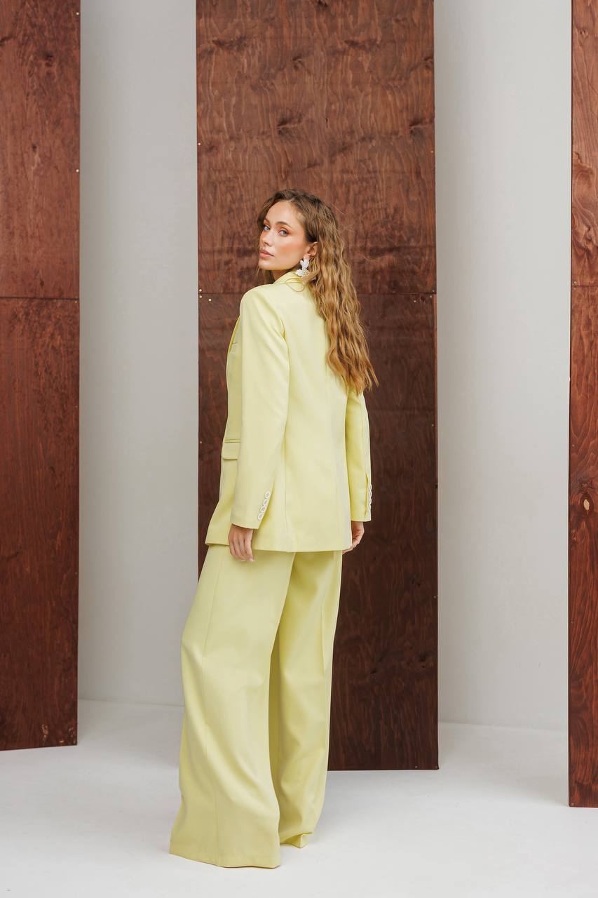 Woman in a light green suit standing against a wooden wall with white columns.