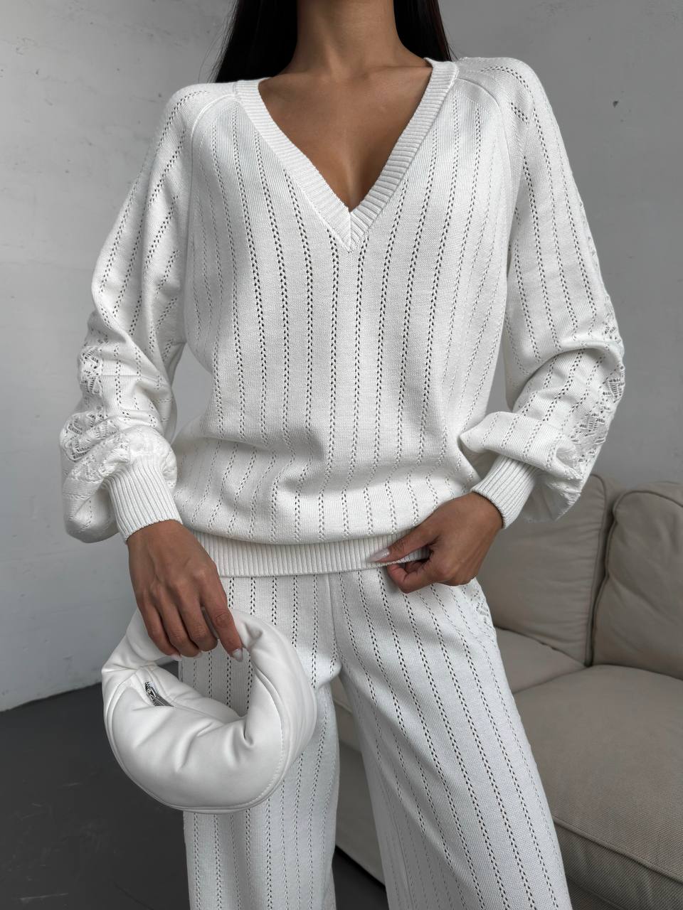 Person wearing a white knit outfit holding a matching handbag against a neutral background