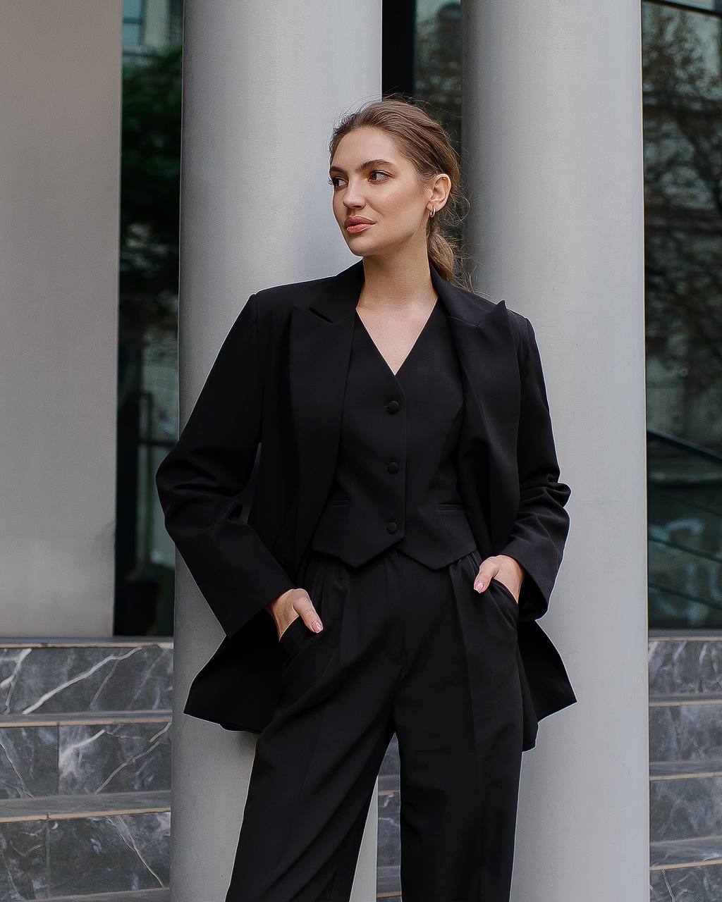 Woman in a black suit standing against a building with columns.