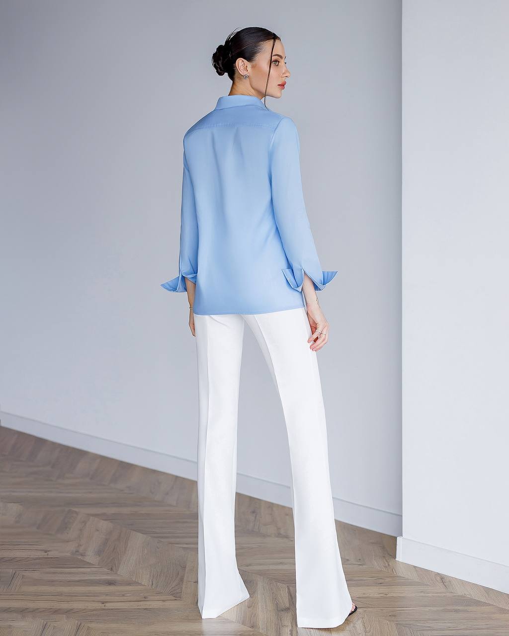 Person wearing a light blue shirt and white pants in a minimalistic setting