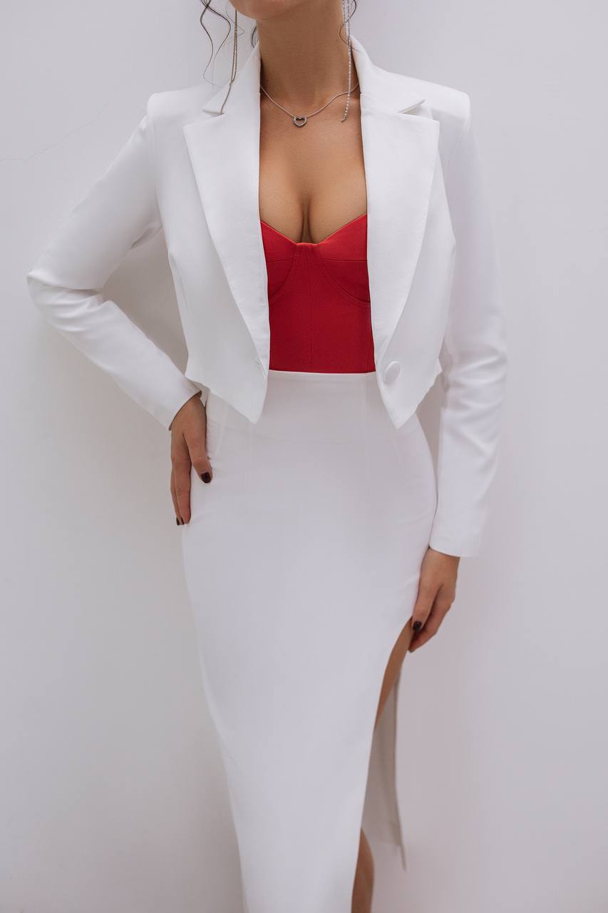 Person wearing a white blazer over a red top and white skirt on a plain background