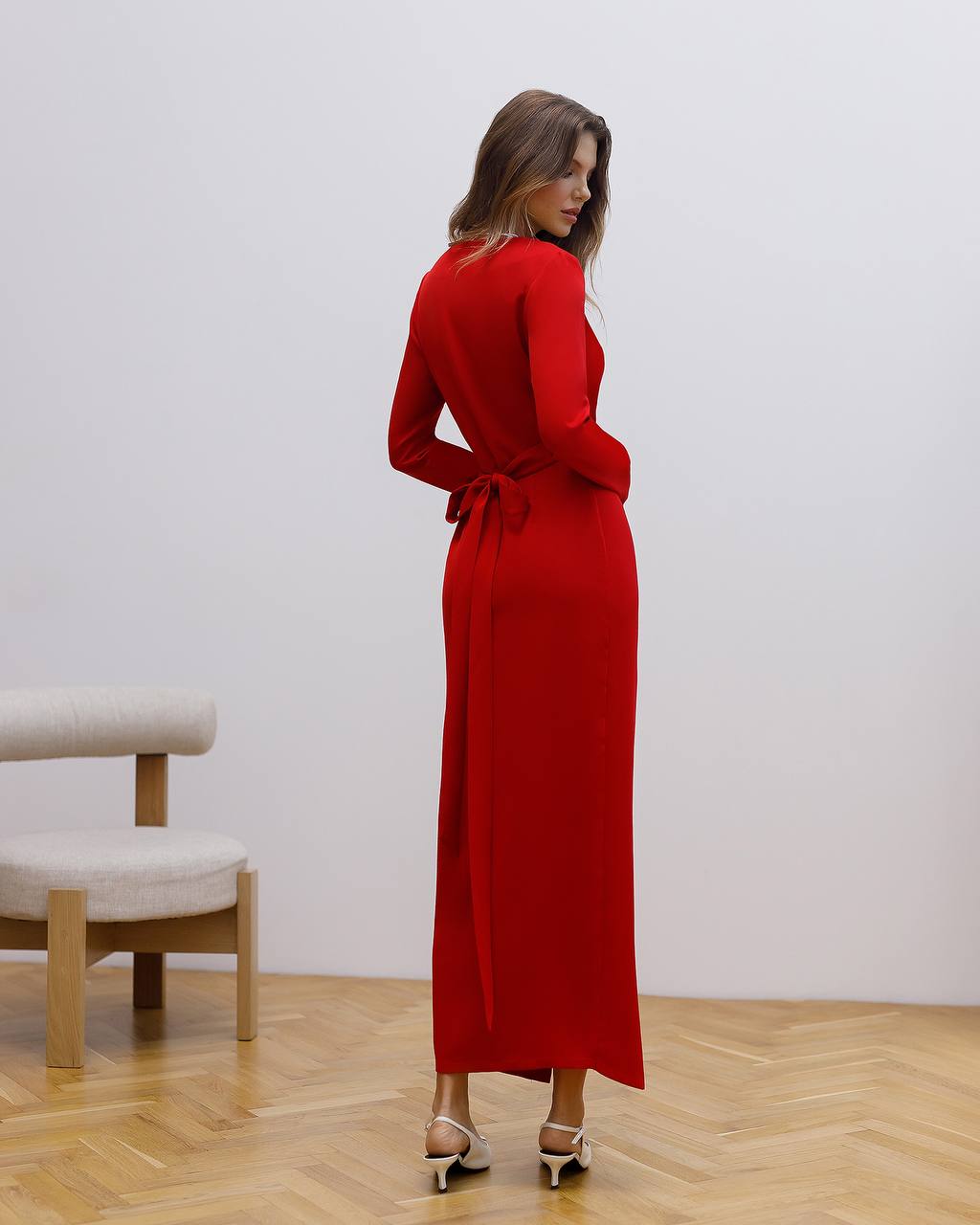 Woman wearing a red dress standing in a room with wooden flooring and a white wall.
