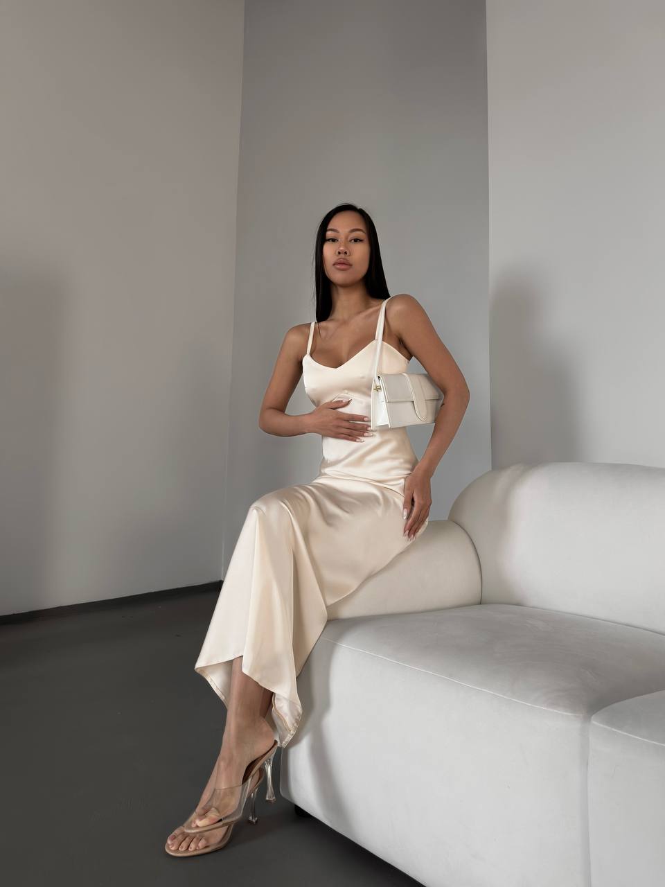 Woman in a beige dress sitting on a white couch against a plain wall.