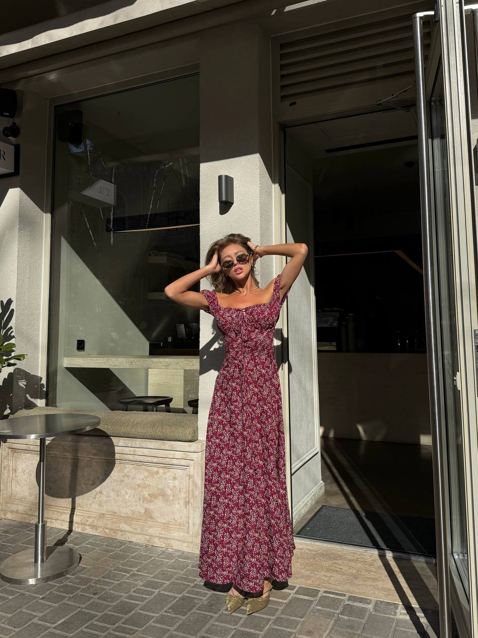 Woman in a floral dress posing outside a modern building.