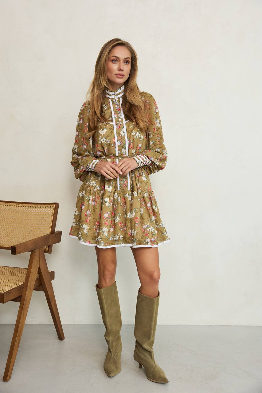 Woman wearing a floral dress and knee-high boots standing in a minimalistic room.