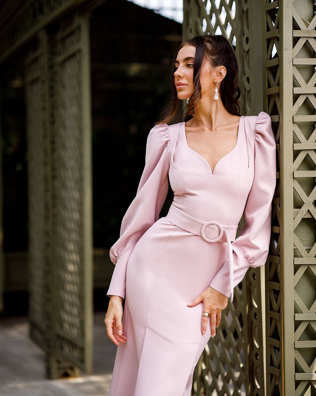 Woman in a pink dress standing against a textured wall.