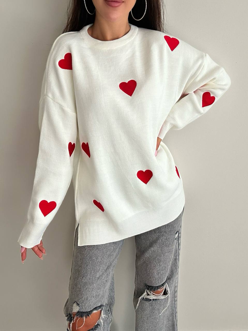 Person wearing a white sweater with red heart patterns on a plain background