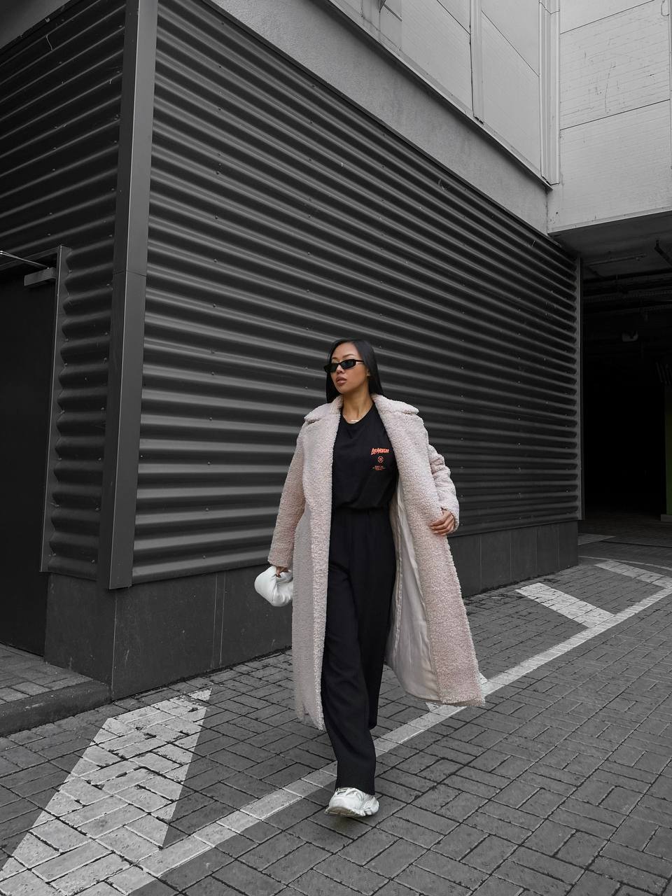Person wearing a long pink coat and black pants walking on a city street.