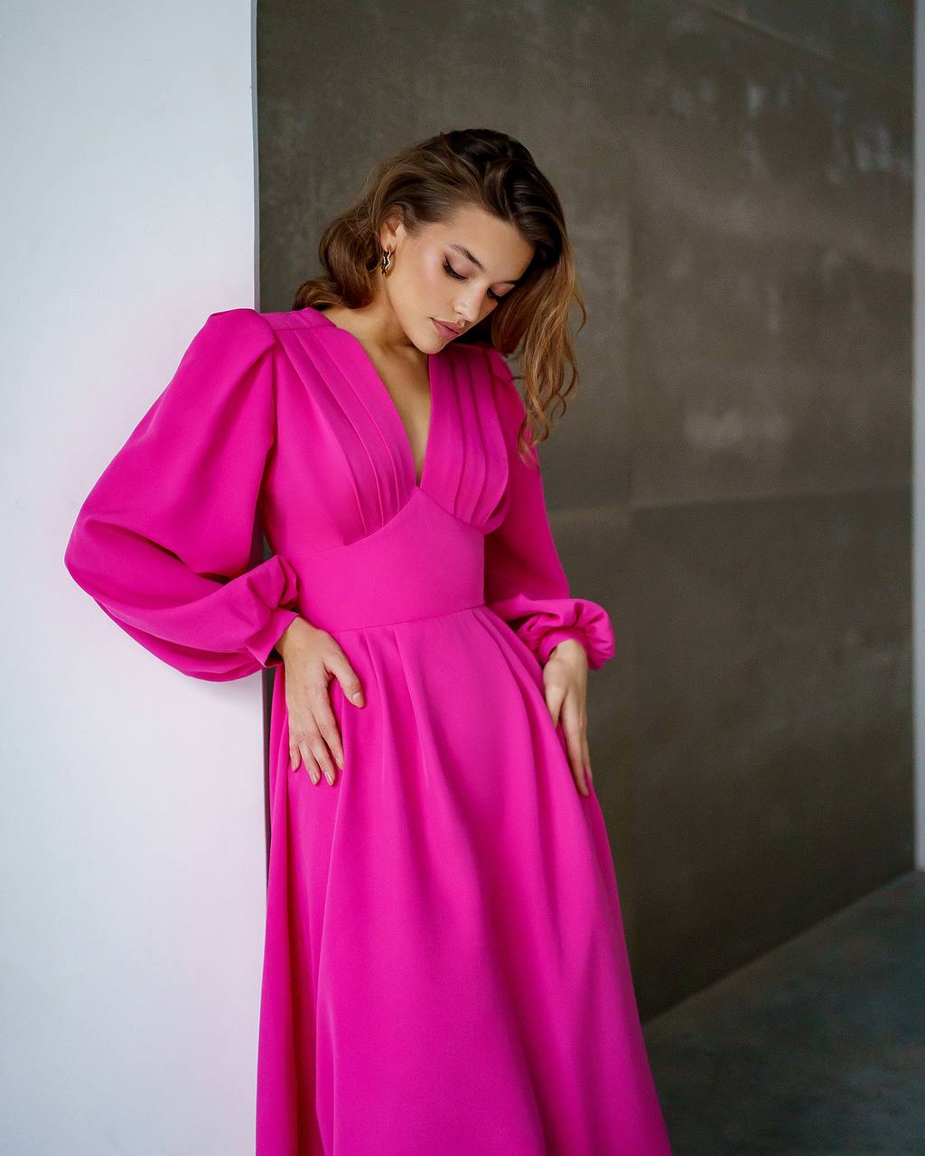 Woman wearing a bright pink dress against a neutral wall.