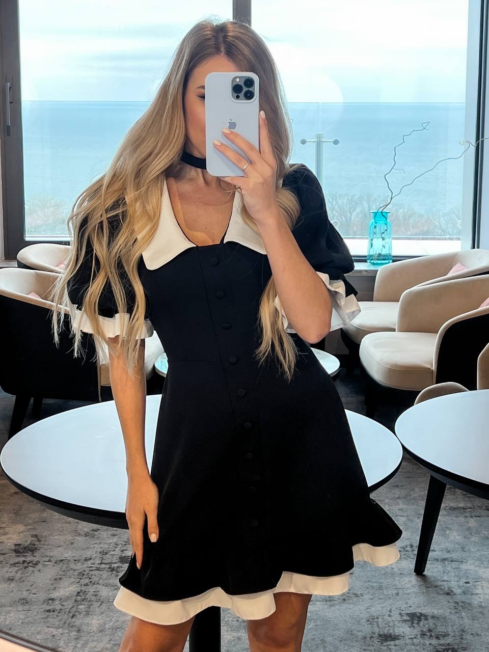 Woman taking a mirror selfie wearing a black and white dress in a modern interior setting.