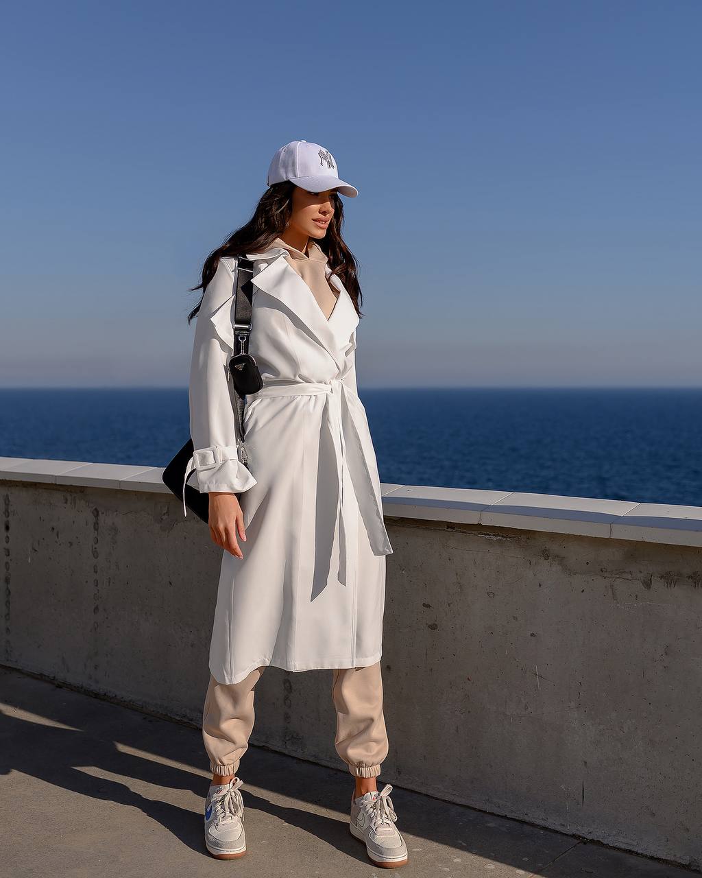 Person wearing a white outfit with a cap, standing by the ocean.