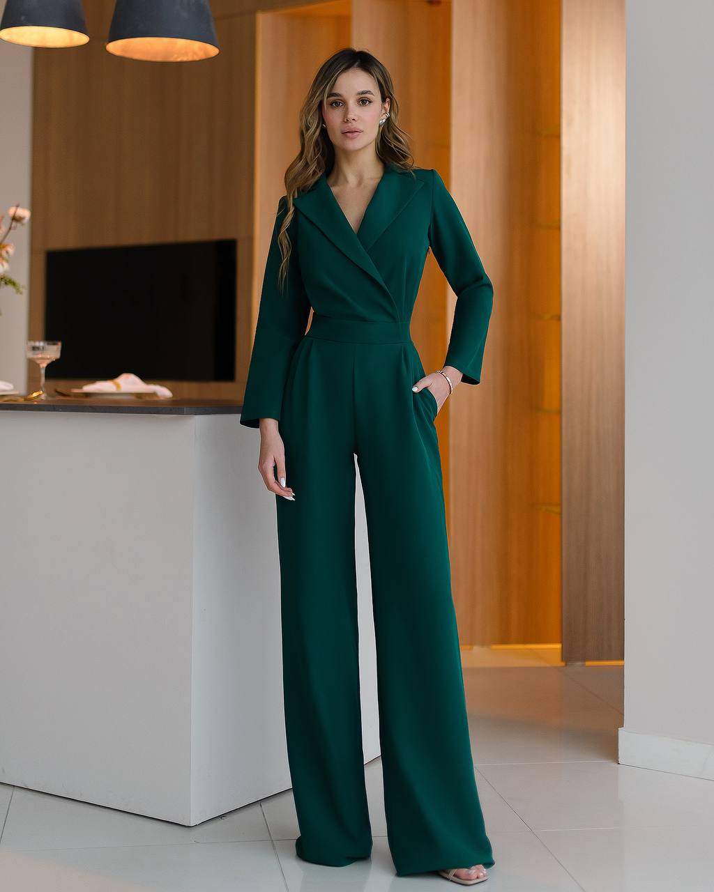 Woman in a green jumpsuit standing in an indoor setting with modern decor.