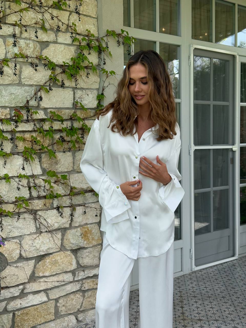 Woman in white outfit standing in front of a stone wall and glass door.