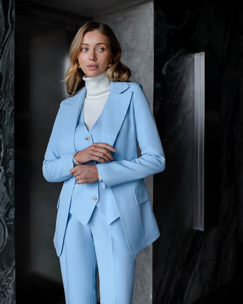 Woman wearing a light blue suit with a white turtleneck against a dark background