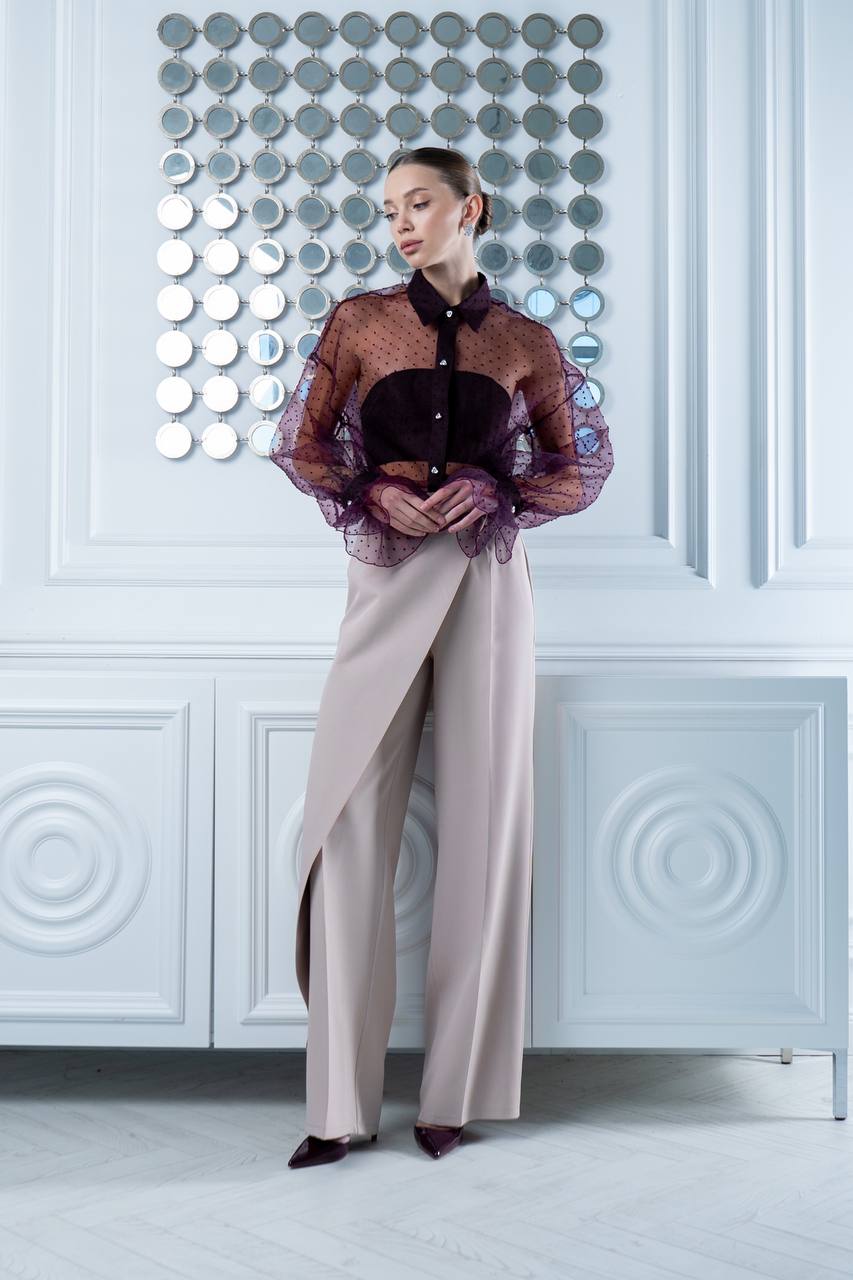 Woman wearing a sheer top and wide-leg pants in a stylish interior setting