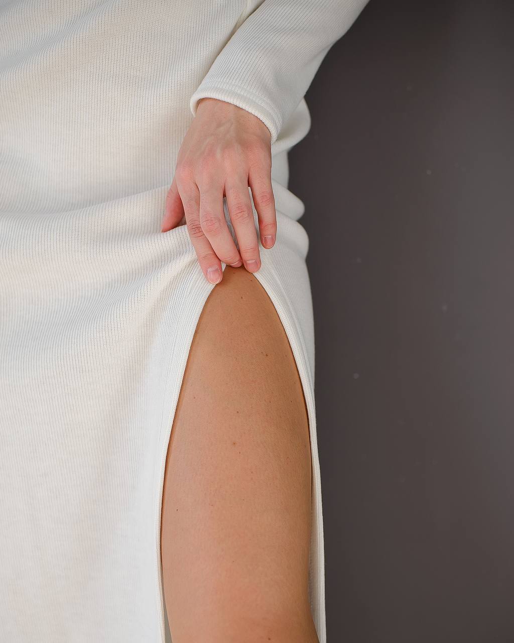 White dress with a high slit and a hand touching the fabric, on a dark background