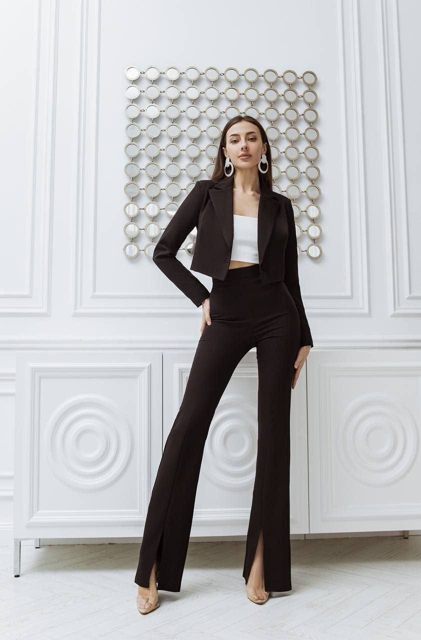 Woman in a black suit standing against a white wall with decorative elements.
