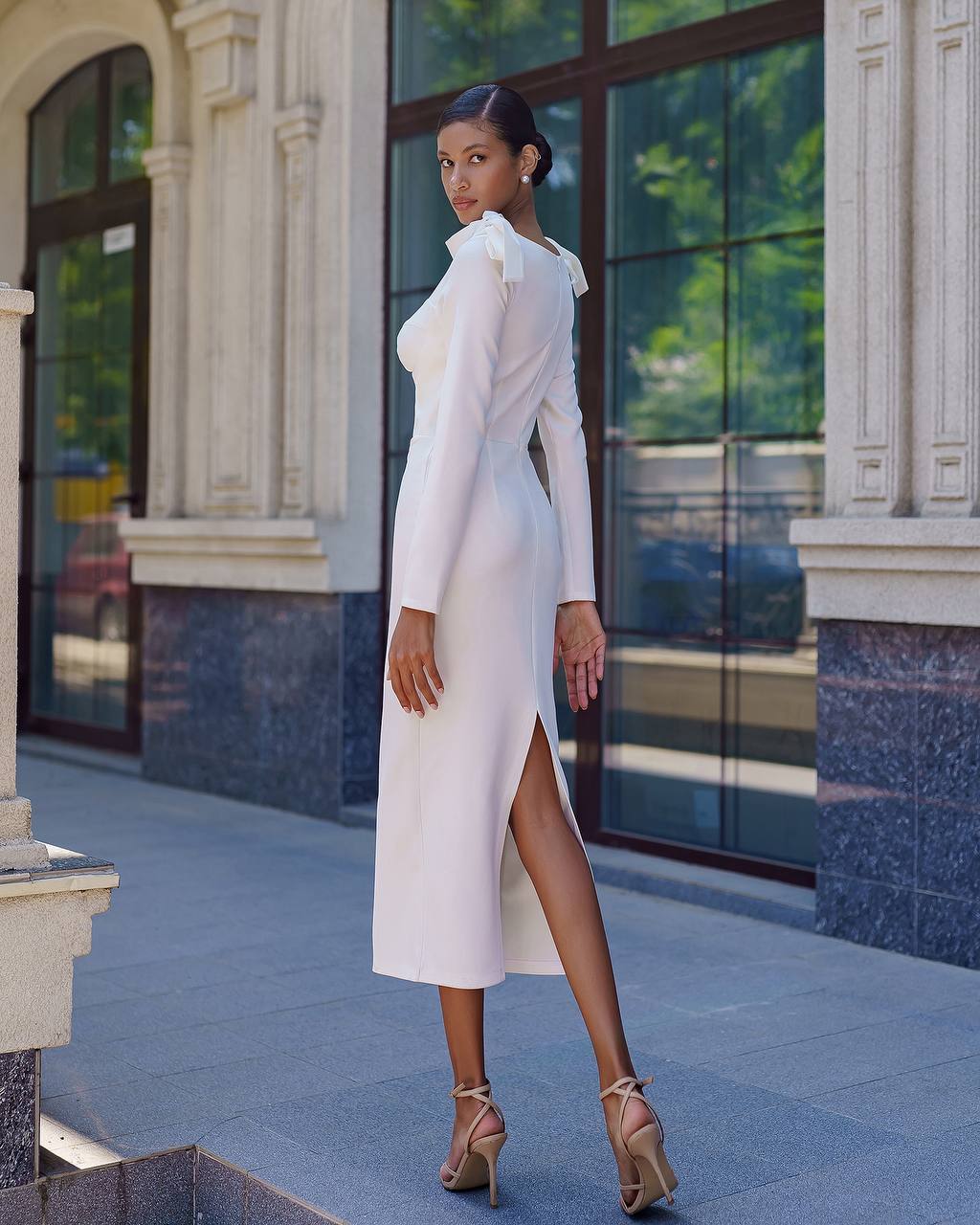 Woman in a white dress standing in front of a building with large windows.