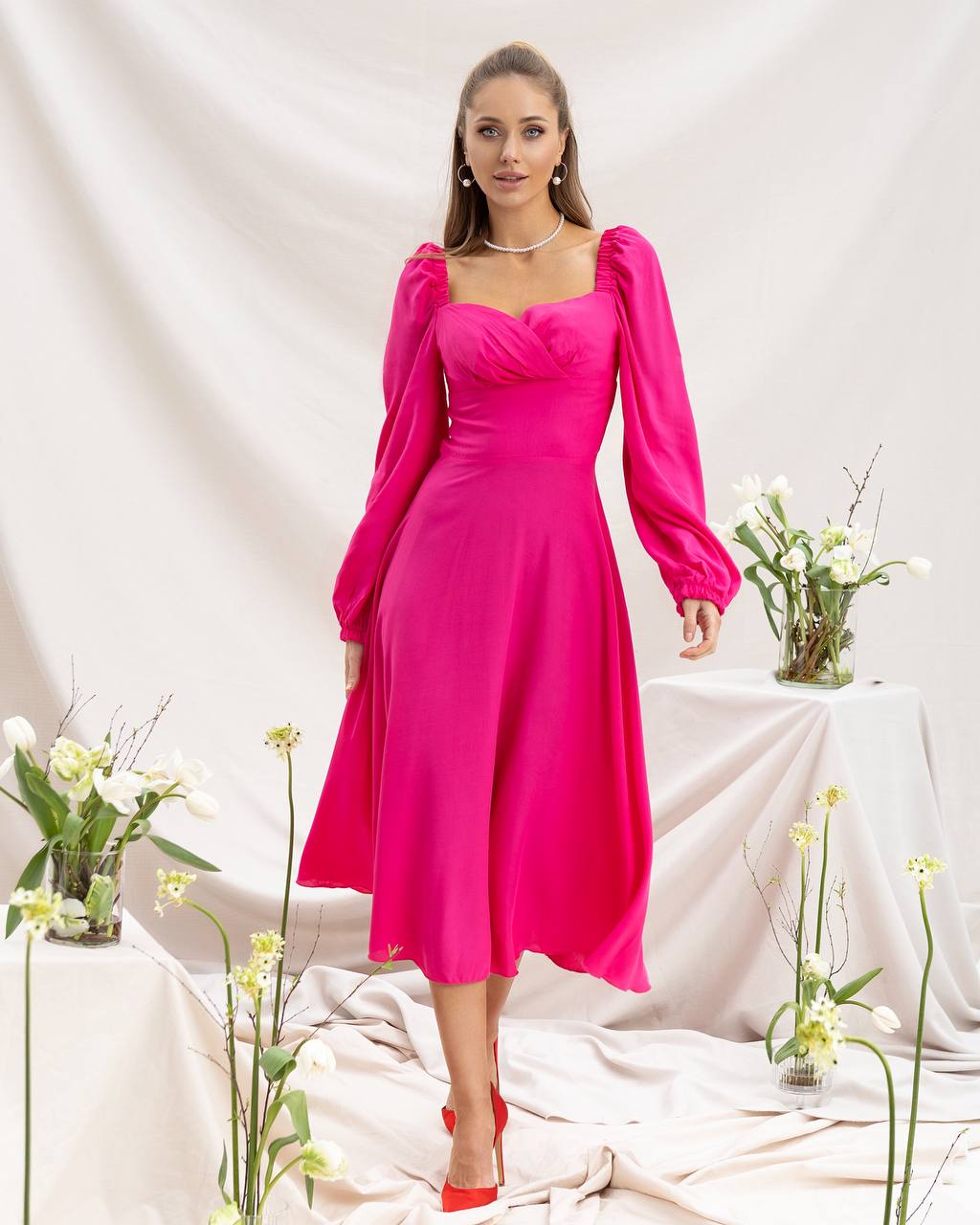 Woman wearing a bright pink dress with long sleeves in a decorated indoor setting.