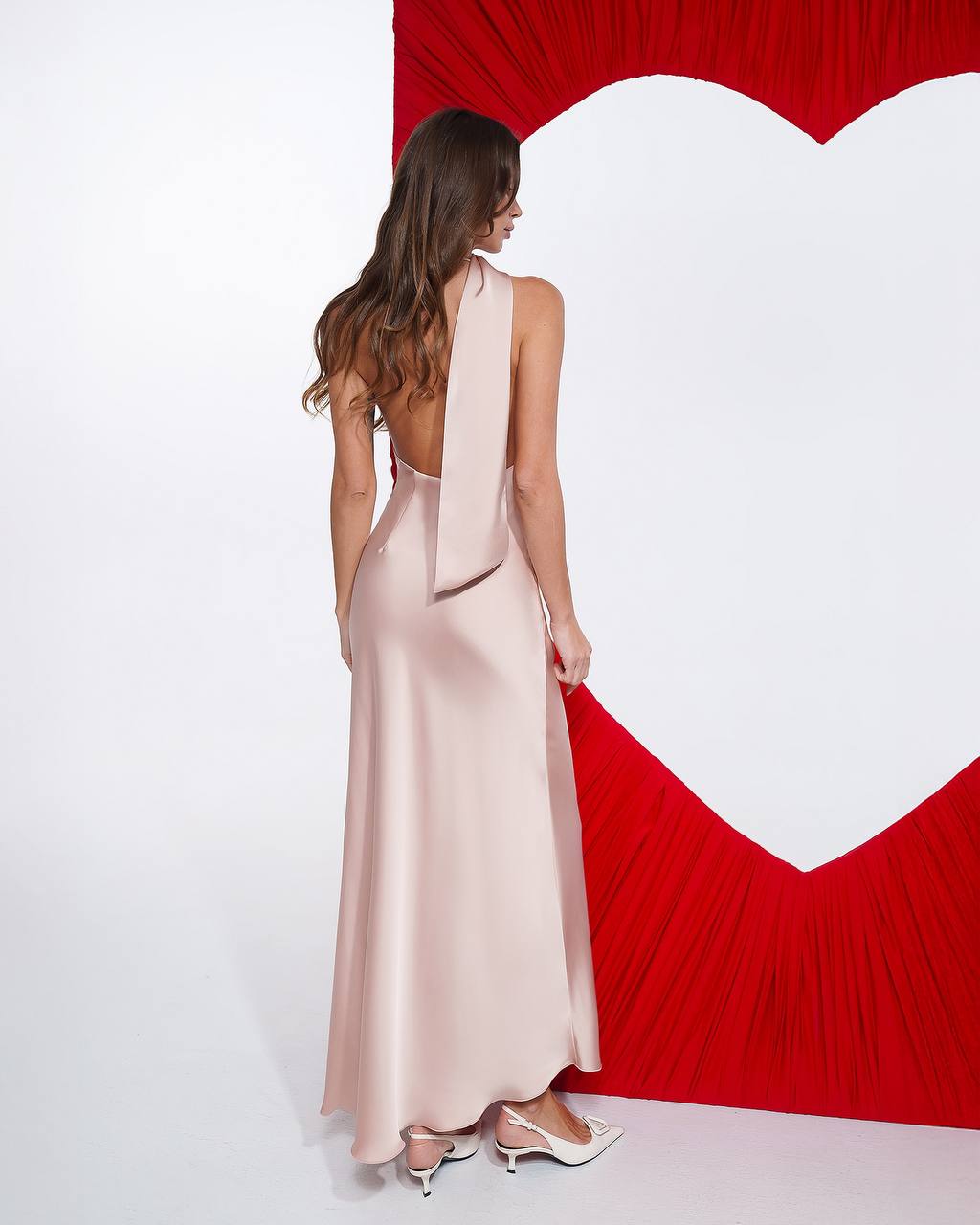 Woman in a pink dress standing in front of a red heart-shaped backdrop