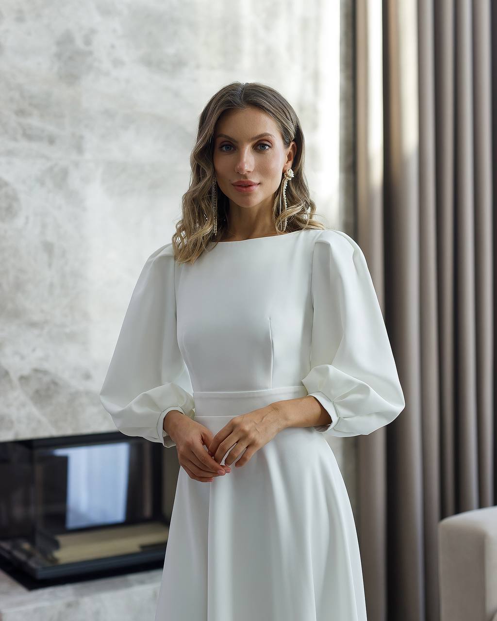 Woman wearing a white dress with puffed sleeves in an indoor setting.
